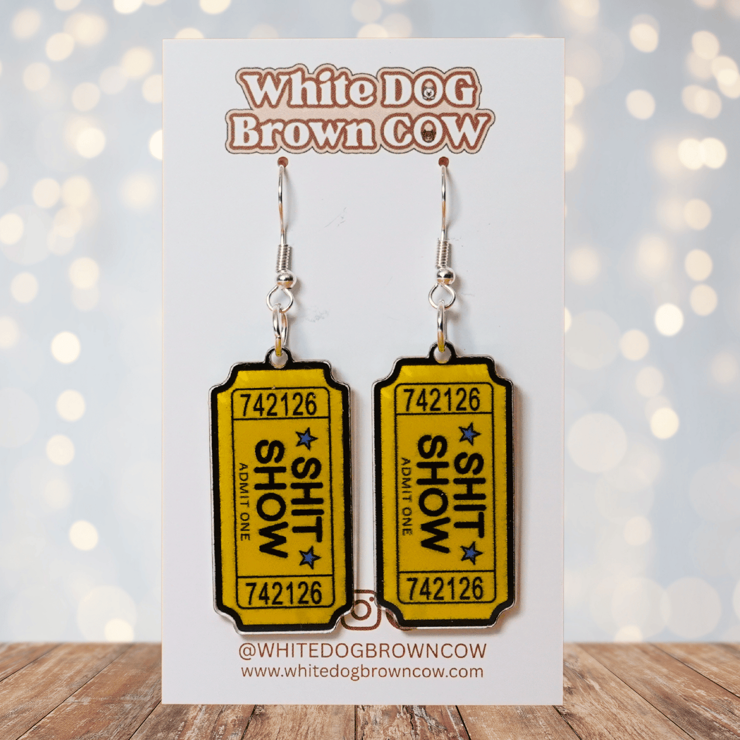 Acrylic dangle earrings designed like yellow admit-one tickets reading “Shit Show”