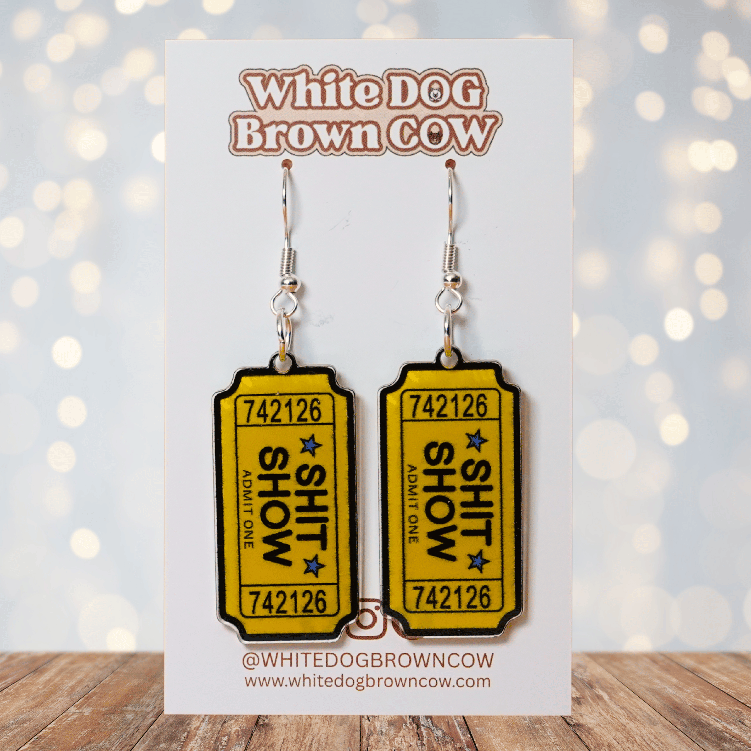 Acrylic dangle earrings designed like yellow admit-one tickets reading “Shit Show”