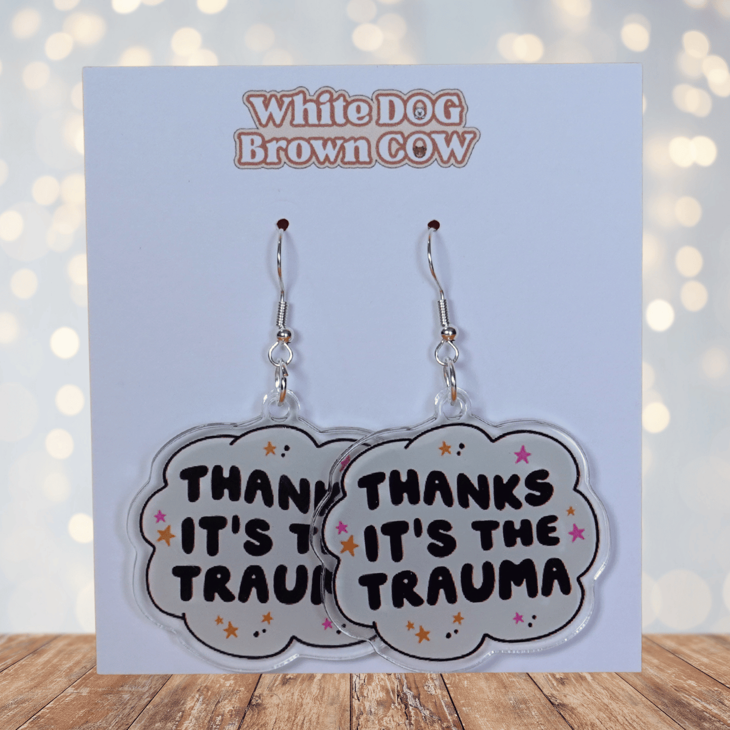 Clear acrylic dangle earrings with a speech bubble shape reading “Thanks it’s the trauma” with small star accents