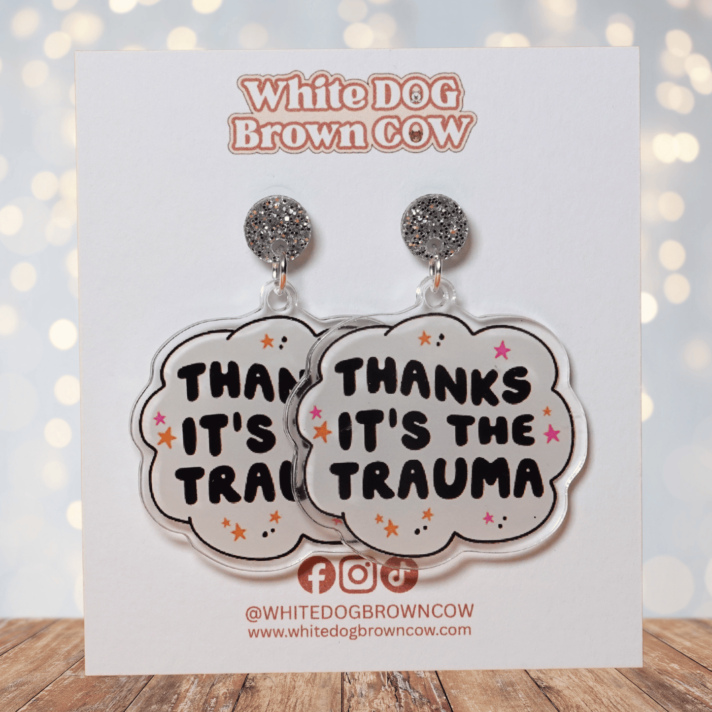 Clear acrylic dangle earrings with a speech bubble shape reading “Thanks it’s the trauma” with small star accents