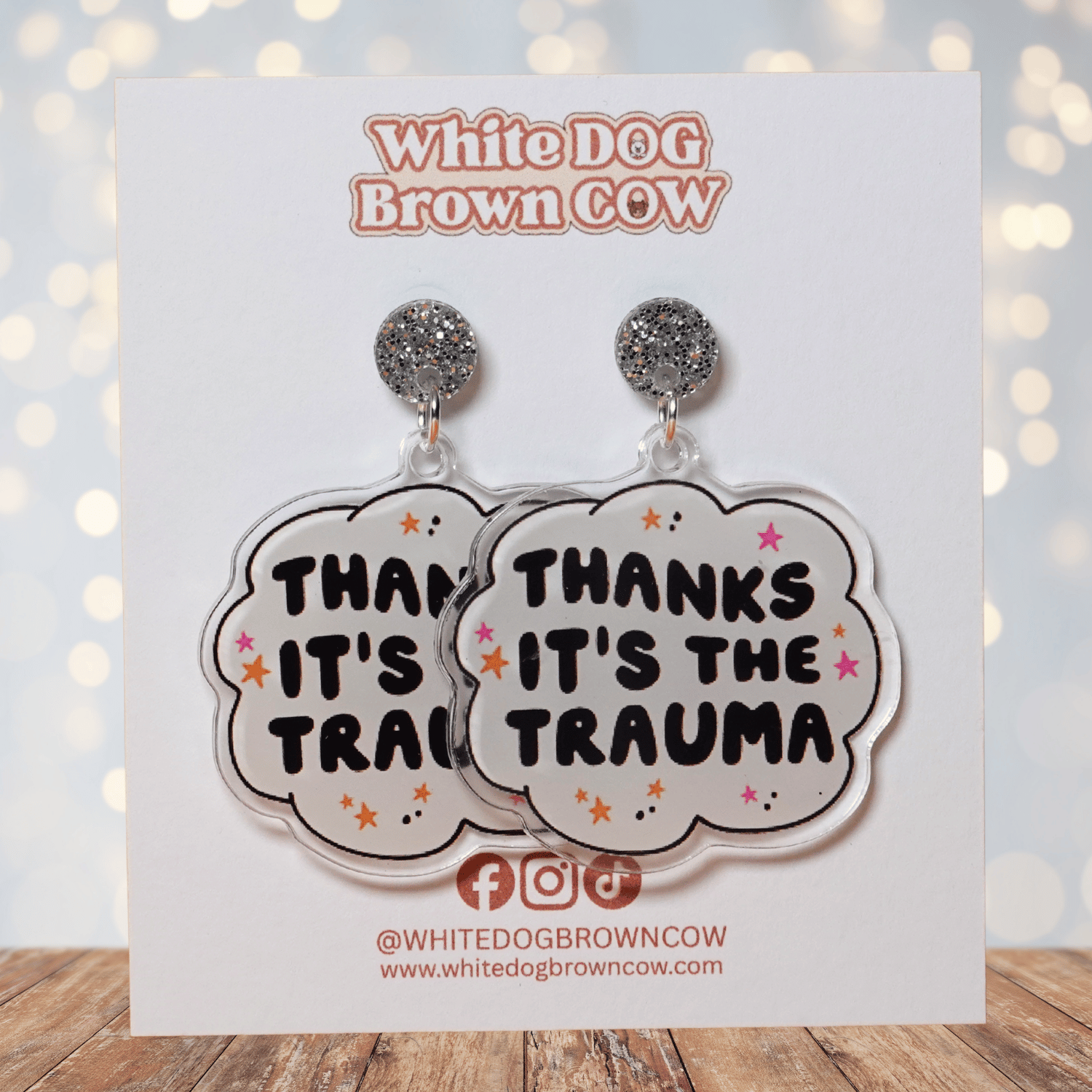 Clear acrylic dangle earrings with a speech bubble shape reading “Thanks it’s the trauma” with small star accents