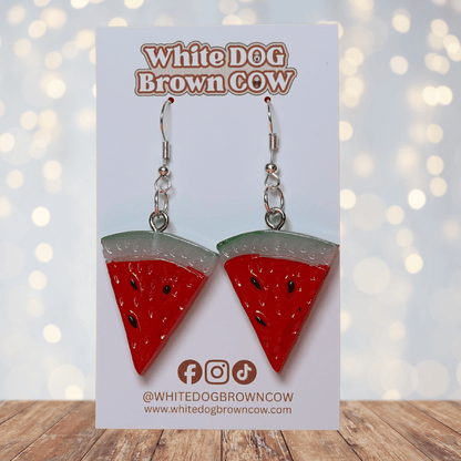 Watermelon slice dangle earrings shaped like red triangular watermelon pieces with green rind and black seed details on silver hooks.