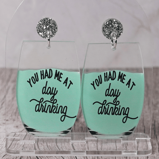 Funny acrylic dangle earrings shaped like wine glasses with mint green drink and text that reads “You had me at day drinking.”